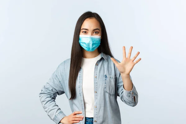 Social distancing livsstil, covid-19 pandemi och människor känslor koncept. Vänlig snygg asiatisk kvinna i medicinsk mask visar nummer fem, gör ordning — Stockfoto