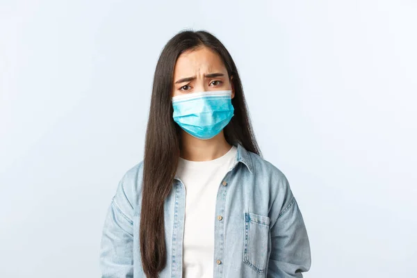 Társadalmi távolságtartó életmód, kovid-19 pandémiás mindennapi élet és szabadidő koncepció. Ideges, komor ázsiai lány orvosi maszkban aggódik, empátiát mutat, ráncolja a homlokát, pozitív lett a koronavírus teszt. — Stock Fotó
