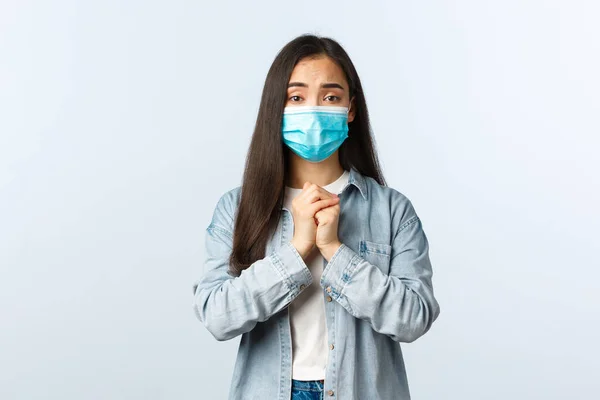 Estilo de vida social distanciamento, covid-19 pandemia vida cotidiana e conceito de lazer. Esperançoso implorando menina asiática pedindo ajuda, aperte as mãos juntas em oração, pedindo favor, use máscara médica — Fotografia de Stock