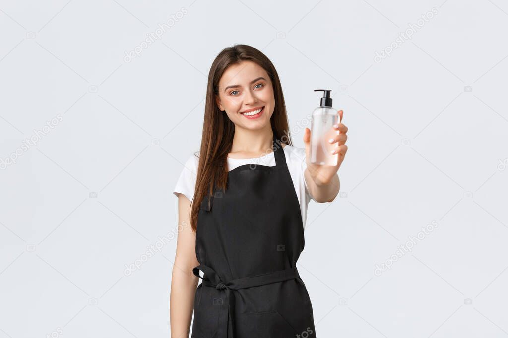 Grocery store employees, small business and coffee shops concept. Friendly cute female barista, saleswoman in black apron suggesting hand sanitizer to visitors with nice smile
