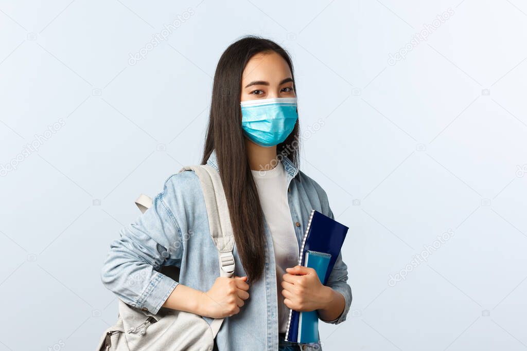 Covid-19 pandemic, education during coronavirus, back to school concept. Stylish modern asian female student at college, carry backpack and notebooks studying material, look camera