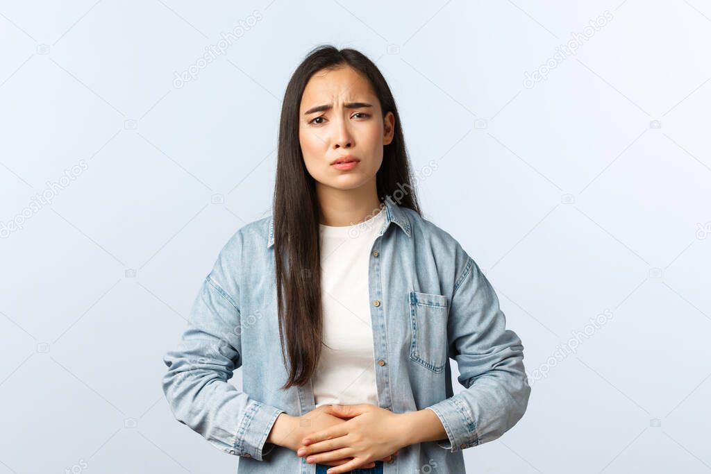 Lifestyle, people emotions and beauty concept. Sick young asian woman having cramps, touching stomach, poisoned in restaurant, grimacing and frowning upset, feeling unwell