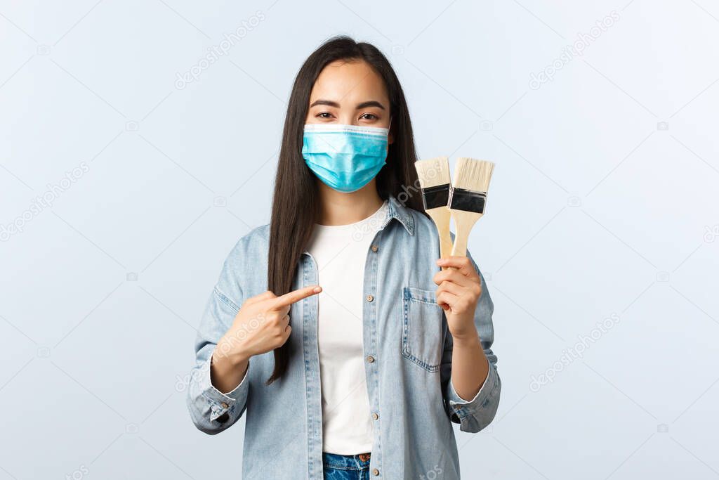 Social distancing lifestyle, covid-19 pandemic, self-isolation hobbies and leisure concept. Cute artistic and creative asian female student plan rebuilding house, showing paint brushes, wear mask