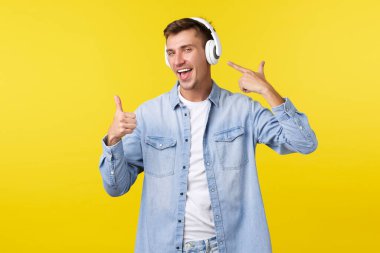 Yaşam tarzı, yaz tatili, teknoloji konsepti. Mutlu yakışıklı adam, kablosuz kulaklıklı öğrenci kulaklıkları işaret ediyor ve iyi müzikten memnun olduğu kadar iyi notalar veriyor, müthiş ritimler.