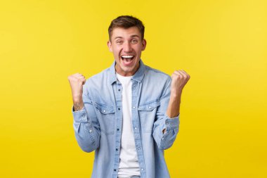 Yaşam tarzı, insan duyguları ve yaz tatili konsepti. Heyecanlı yakışıklı mutlu adam seviniyor, elini kaldırıyor ve şarkı söylüyor, takımı destekliyor, şampiyon oluyor, sarı arka planda zafer kazanıyor.