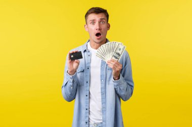 Şok olmuş ve afallamış, sıradan giyinmiş sarışın yakışıklı, kararsız, nasıl yatırım yapacağını bilmeyen, kredi kartı ve para gösteren, sarı arka planda duran,