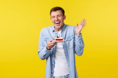 Kutlamalar, tatiller ve insanların duyguları. Partide doğum gününü kutlayan neşeli ve şaşırmış adam. Kahkaha ve neşe dolu gülümseme, doğum günü pastası tabağı, sarı arka plan