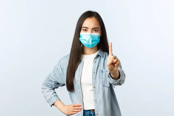 Social distanslivsstil, covid-19 pandemisk vardag och fritidskoncept. Arg missnöjd asiatisk flicka i medicinsk mask scolding person, visa fingret, förbjuda eller varna någon — Stockfoto