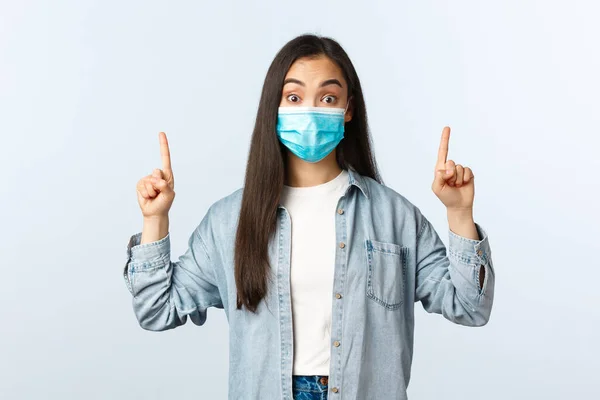 Social distanslivsstil, covid-19 pandemisk vardag och fritidskoncept. Förvånad och intresserad kvinnlig student i medicinsk mask höra om nya intressanta program, peka finger upp — Stockfoto