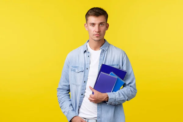 Education, courses and university concept. Serious-looking college student, guy with notebooks, looking determined camera, casual expression as heading to class, yellow background