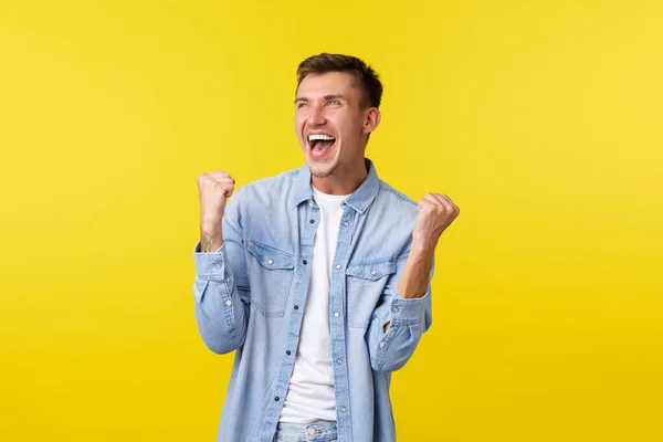 Estilo de vida, emoções das pessoas e conceito de lazer de verão. Homem louro bonito feliz levantando as mãos e gritando sim, sentindo-se feliz como triunfante, aposta vencedora, jogo sobre fundo amarelo — Fotografia de Stock