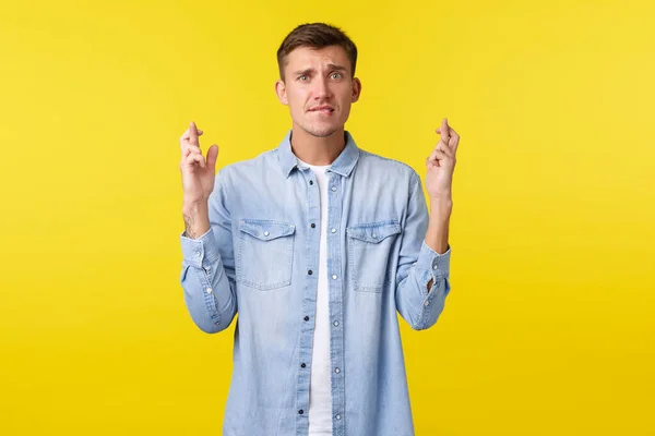 Mode de vie, émotions des gens et concept de loisirs d'été. Blond anxieux beau mec inquiet de son avenir, les doigts croisés et la lèvre mordante comme faire un voeu, en attente de résultats importants, fond jaune — Photo