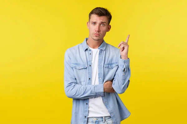 Sérieux beau gay homme en chemise en denim, lever l'index ont suggestion, dire son idée ou plan, trouvé une bonne solution, debout fond jaune déterminé — Photo