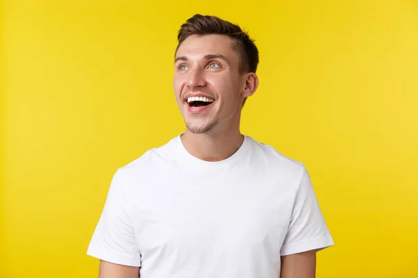 Lifestyle, zomer en mensen emoties concept. Dromerige knappe vrolijke man in casual wit t-shirt, op zoek linksboven hoek blij en glimlachend met witte tanden, gele achtergrond — Stockfoto