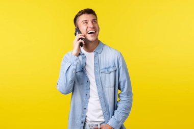 Teknoloji, yaşam tarzı konsepti. Neşeli, yakışıklı, gülümseyen adam telefonda mutlu bir konuşma yapıyor, arkadaşını arıyor, hevesli görünüyor ve akıllı telefonu kulağının dibinde tutuyor, sarı arka planda.