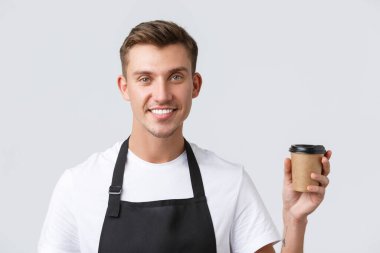 Kafe ve restoranlar, kafe sahipleri ve perakende konsepti. Yakından çekilen yakışıklı barista, garsonun müşteriye servis yaptığı içecek, elinde kağıt bardak ve gülümseyen beyaz arka plan.