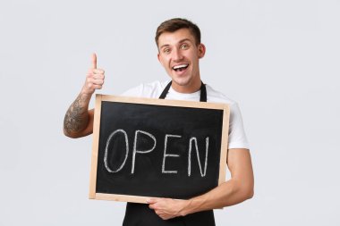 Küçük perakende şirketleri, kafe ve restoran çalışanları konsepti. Dostça gülümseyen barista, garson ya da satıcı açık tabela ve baş parmak işareti gösteriyor, mağazayı ziyaret etmeye davet ediyor, beyaz arka plan