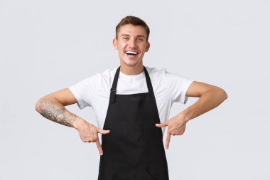 Küçük işletme sahipleri, kahve dükkanı ve personel konsepti. Dost canlısı, neşeli barista, misafirleri davet ediyor, parmaklarını aşağı gösteriyor ve gülümsüyor reklam yapıyor gibi, afiş ve anonsla