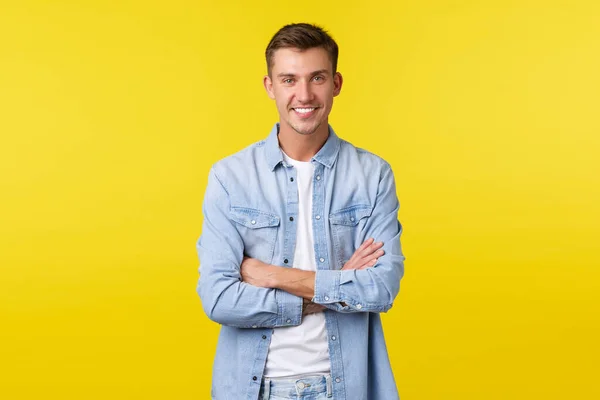 Retrato de guapo chico caucásico feliz con dientes blancos, sonriendo ampliamente, brazos cruzados pecho seguro, de pie fondo amarillo en camisa de mezclilla sobre camiseta blanca —  Fotos de Stock