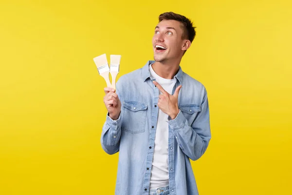 Hobbies, ocio y gente concepto de estilo de vida. Entusiasta guapo rubio chico señalando los dedos esquina superior izquierda en la bandera promocional con materiales de construcción, la celebración de pinceles — Foto de Stock