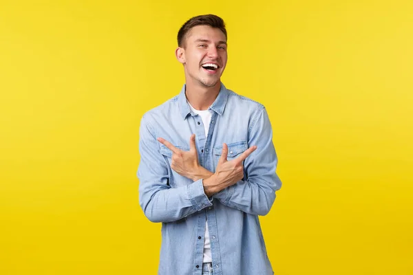 Portret van een charismatische knappe blonde man die vrolijk lacht en zijwaarts wijst, links en rechts varianten of producten toont, vrolijk over een gele achtergrond staat — Stockfoto