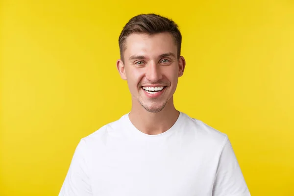 Estilo de vida, verano y personas concepto de emociones. Modelo masculino guapo entusiasta con sonrisa feliz y dientes blancos, de pie en camiseta casual sobre fondo amarillo satisfecho —  Fotos de Stock