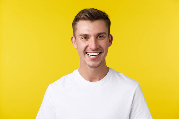 Lifestyle, summer and people emotions concept. Enthusiastic handsome male model with happy smile and white teeth, standing in casual t-shirt over yellow background satisfied