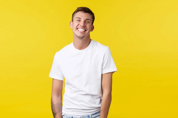 Stile di vita, estate e persone emozioni concetto. Bello carismatico caucasico ragazzo in casual t-shirt bianca sorridente ampiamente con perfetto sorriso bianco, in piedi gioioso sfondo giallo — Foto Stock