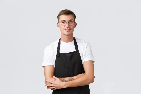 Small retail business owners, cafe and restaurant employees concept. Handsome barista, salesman in glasses and black apron, listening customer, waiter taking order, white background — Stock Photo, Image