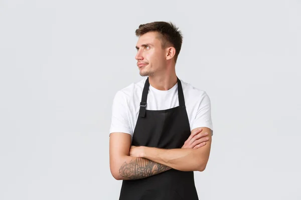 Empregados, mercearias e conceito de café. Barista mal-humorado descontente, trabalhador do café em avental preto sentindo-se louco ou ofendido, vire as costas amuado e cruz braços peito, fundo branco — Fotografia de Stock