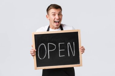 Küçük perakende şirketleri, kafe ve restoran çalışanları konsepti. Neşeli gülümseyen barista misafirleri selamlıyor, pazarlamacı açık tabela olduğumuzu gösteriyor ve gülümseyen neşeli, beyaz arka plan