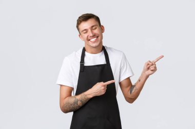 Küçük işletme sahipleri, kahve dükkanı ve personel konsepti. Mutlu, aptal, gülümseyen, yakışıklı barista, önlüklü garson, gözleri kıpkırmızı, sevinç içinde, tam da tatmin edici haberleri işaret eden.