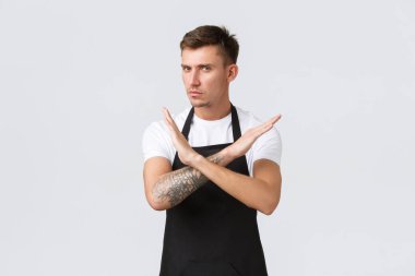 Çalışanlar, bakkallar ve kahve dükkanı konsepti. Siyah önlüklü, hayal kırıklığına uğramış barista, garson ya da kafe çalışanı. Hareketi durdurmak, uyarmak ya da onaylamamak için çapraz işaret yapıyor.