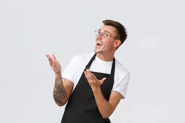 Small retail business owners, cafe and restaurant employees concept. Surprised and happy barista, salesman in black apron and glasses pointing and looking delighted upper left corner — Stock Photo, Image