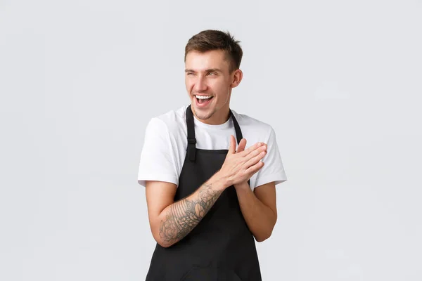 Small business owners, coffee shop and staff concept. Devious and smart funny barista in black apron, cafe worker rubbing hands as expect relish or satisfaction from accomplished plan, grinning sly — Stock Photo, Image