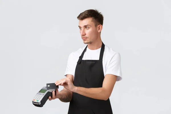 Negocio minorista, cafetería y restaurante, concepto de empleados. Barista guapo en delantal negro, camarero entregando terminal de punto de venta para pago y tarjeta de crédito, sirviendo orden a los clientes — Foto de Stock