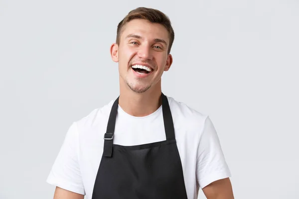 Cafe and restaurants, coffee shop owners and retail concept. Close-up of cheerful handsome salesman in black apron inviting or welcoming clients in store, laughing happy, white background — Stock Photo, Image