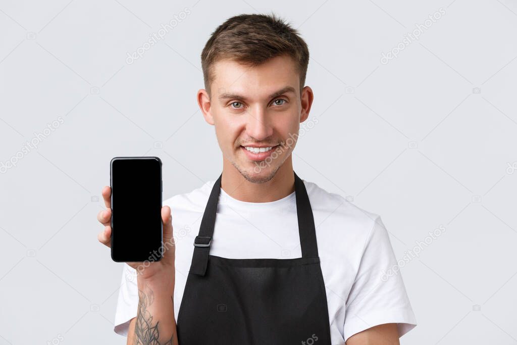 Cafe and restaurants, coffee shop owners and retail concept. Close-up of cheeky handsome salesman inform people new app for online orders, showing smartphone display and smiling