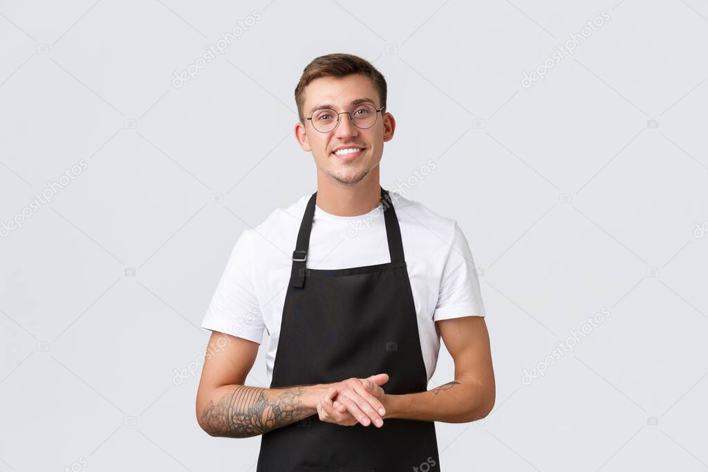 Small retail business owners, cafe and restaurant employees concept. Cheerful friendly-looking barista in black apron, waiter wearing glasses and smiling to client, serving tables, white background