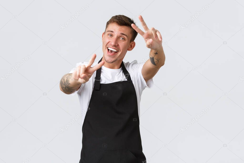 Employees, grocery stores and coffee shop concept. Friendly handsome hipster guy working in cafe, waiter send positive vibes, welcome guests with peace signs, smiling happy