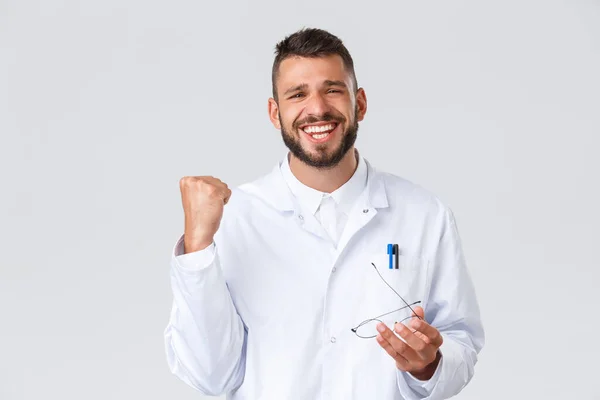 Healthcare workers, coronavirus, covid-19 pandemic and insurance concept. Relieved happy doctor in white scrubs, take-off glasses and fist pump rejoice, winning, celebrating victory — Stock Photo, Image