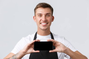 Kafe ve restoranlar, kafe sahipleri ve perakende konsepti. Akıllı telefon görüntüsü ve gülümseme sergileyen neşeli ve yakışıklı satış elemanının yakın plan çekimi, menajer müşterilerine yeni uygulama, özel indirimler