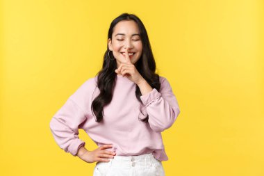 İnsan duyguları, yaşam tarzı ve moda kavramı. Şirin Koreli kız susuyor ve gülümsüyor. Gözleri kapalı, sırlarını saklıyor. Sessiz ol, sürpriz gibi hazırlan, sarı arka planda dur.