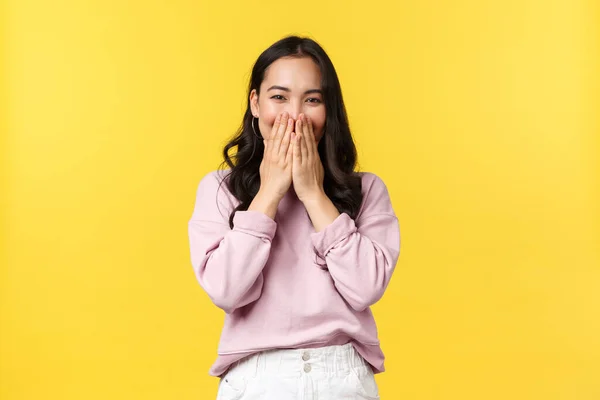 People emotions, lifestyle and fashion concept. Funny and cute korean woman laughing shy, smiling with eyes while cover mouth and giggle silly at camera, standing yellow background