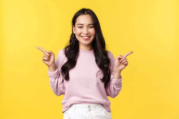 As pessoas emoções, estilo de vida e conceito de moda. Mulher asiática alegre sorrindo e mostrando ambos os produtos, apontando os dedos lateralmente para duas ofertas ou banners sobre fundo amarelo — Fotografia de Stock