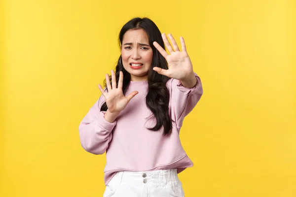 Gente emociones, estilo de vida y concepto de moda. Alarmada y disgustada mujer asiática levantando las manos defensiva, pidiendo parar, sintiéndose ansiosa y asustada de pie fondo amarillo —  Fotos de Stock