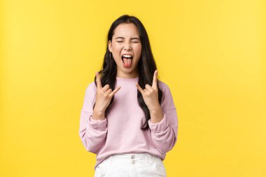 Yaşam tarzı, duygular ve reklam konsepti. Kaygısız ve neşeli Koreli kız harika bir konserde eğleniyor, kapalı gözler dilini ve rock hareketini gösteriyor, müzikten hoşlanıyor, sarı arka plan