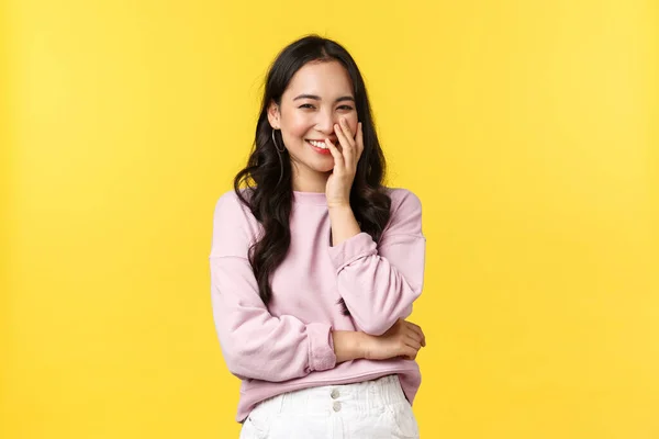 Életmód, érzelmek és reklám koncepció. Gyönyörű és boldog romantikus ázsiai lány vihog, tartsa a kezét a száját, miközben mosolyog, nézi valami imádnivaló és buta, sárga háttér — Stock Fotó