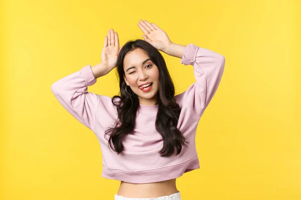 Estilo de vida, emociones y concepto de publicidad. Linda y tonta chica asiática haciendo orejas de conejo de manos y bailando, mirando kawaii con radiante sonrisa blanca, sentirse feliz de pie fondo amarillo —  Fotos de Stock