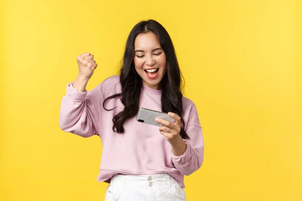 People emotions, lifestyle leisure and beauty concept. Enthusiastic asian girl gamer playing on mobile phone, tilting smartphone to pass level in game, smiling amused, fist pump as winning — Stock Photo, Image